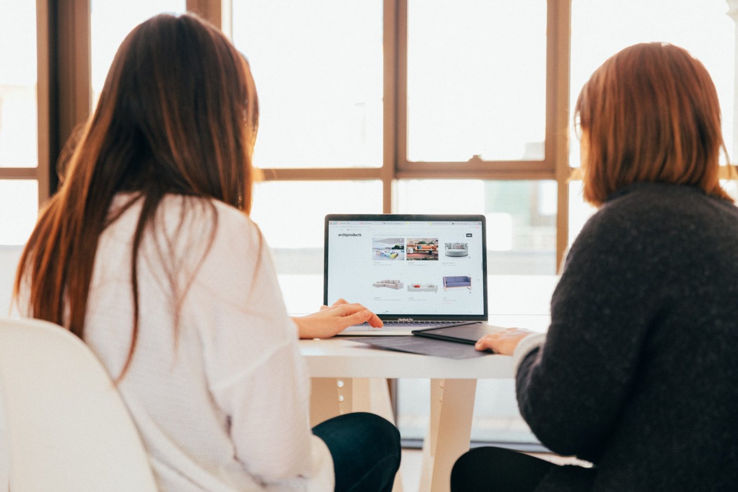 Dos mujeres de espalda trabajando en una oficina con una computadora